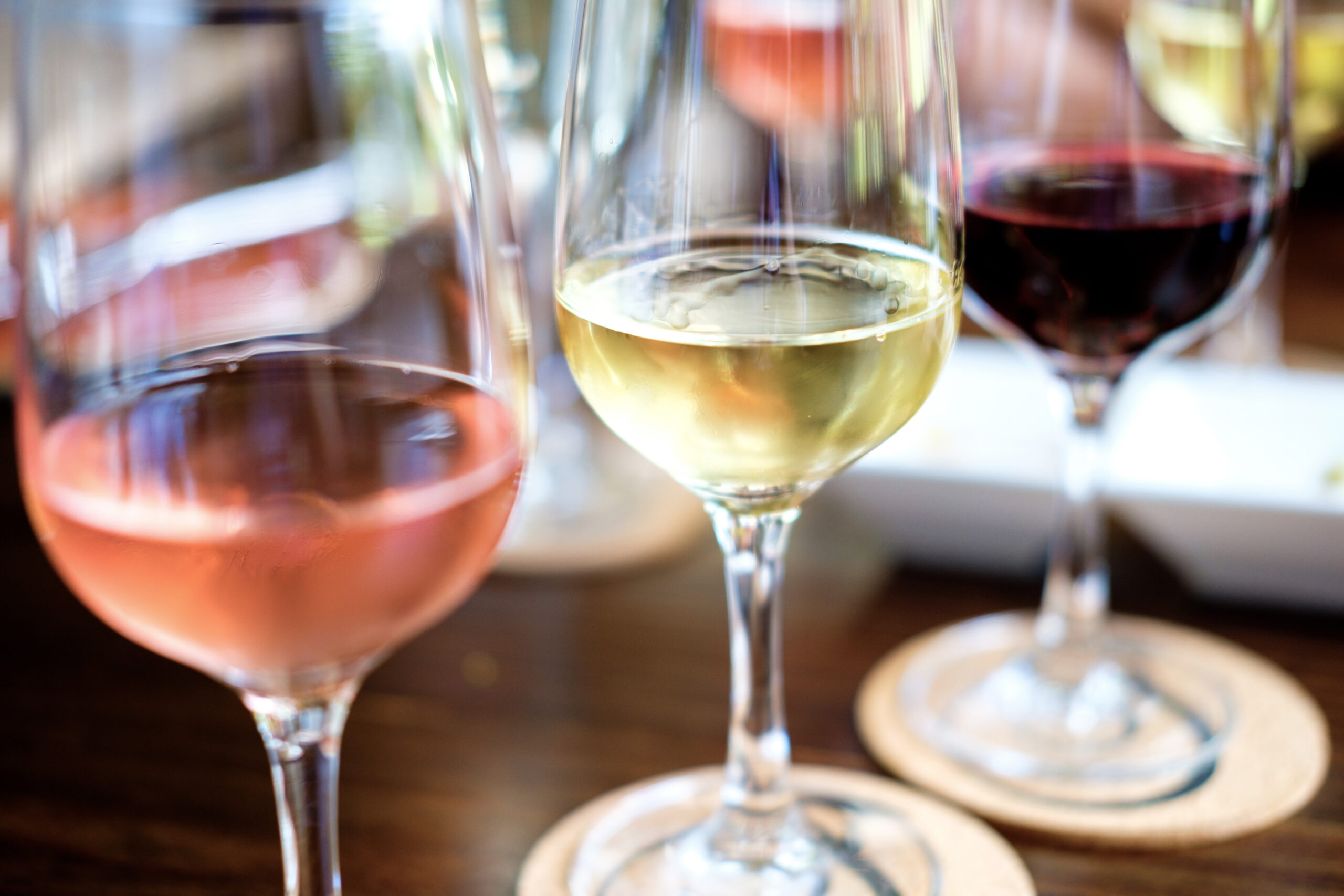 Drei Weingläser, die mit Weißwein, Rotwein und Rosé-Wein gefüllt sind. Sie stehen auf einem Holztisch.
